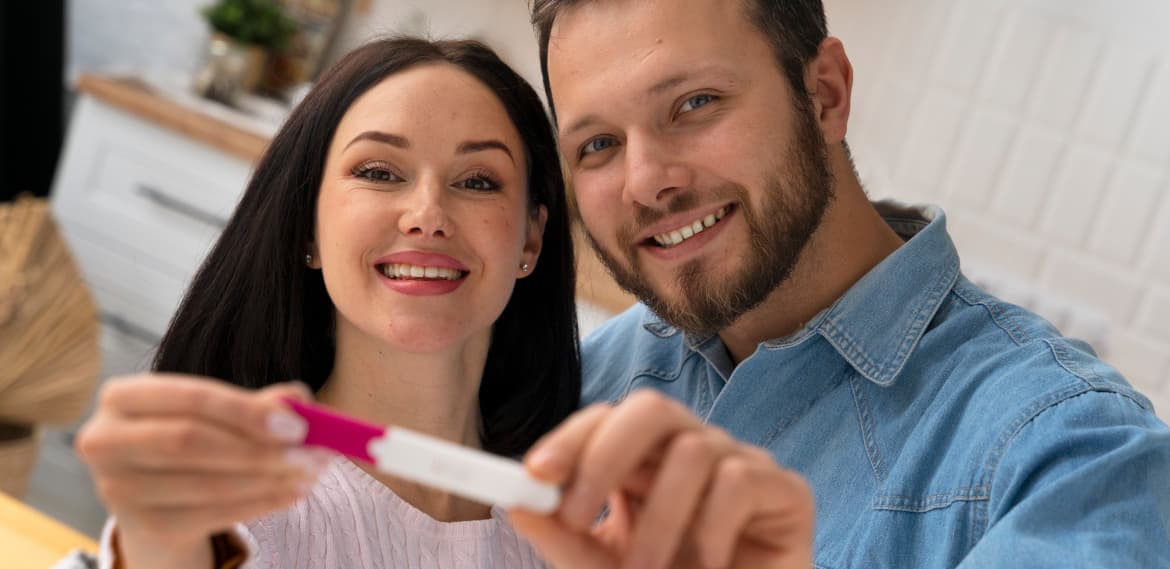 Una pareja sonriente muestra su prueba de embarazo positiva